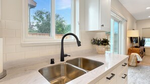 A kitchen with a double sink, white cabinets, and a window providing a view of trees.