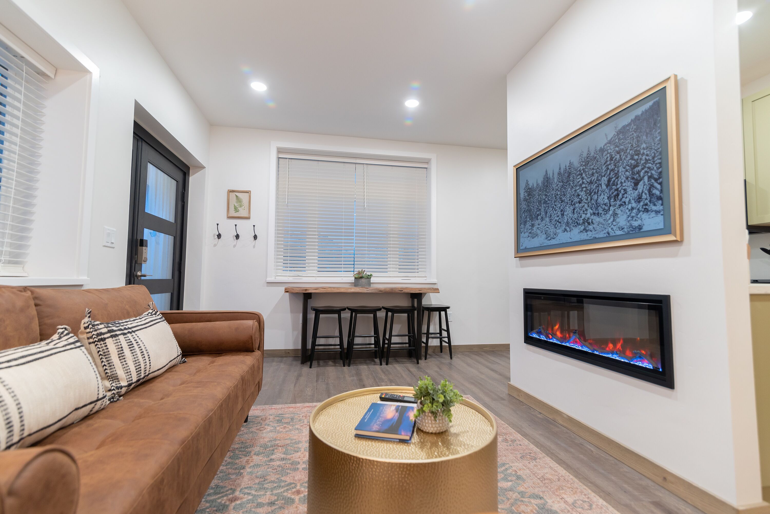 A modern living room with a brown sofa, a round coffee table with a book and a plant, a fireplace, and a large framed picture on the wall.
