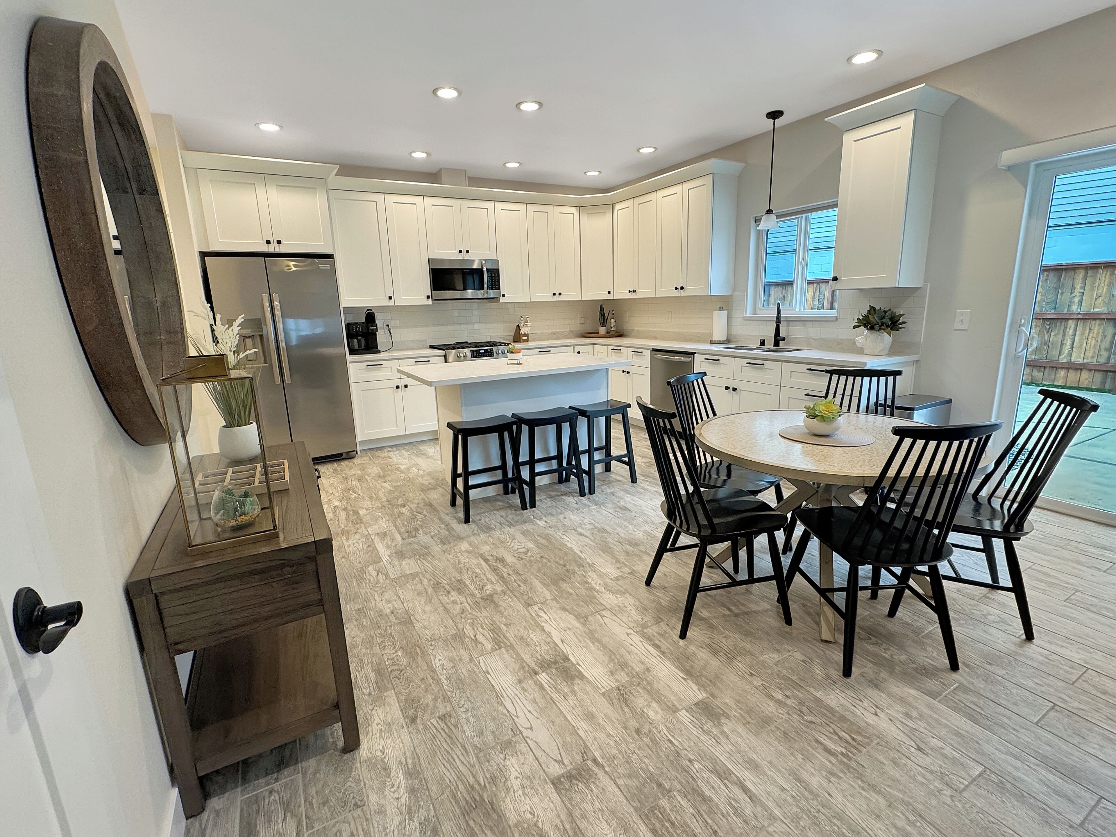 A modern kitchen with white cabinets, a central island, and a dining area with black chairs.