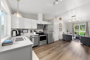 Una cocina moderna con electrodomésticos de acero inoxidable, una isla grande y un comedor con sofá gris.