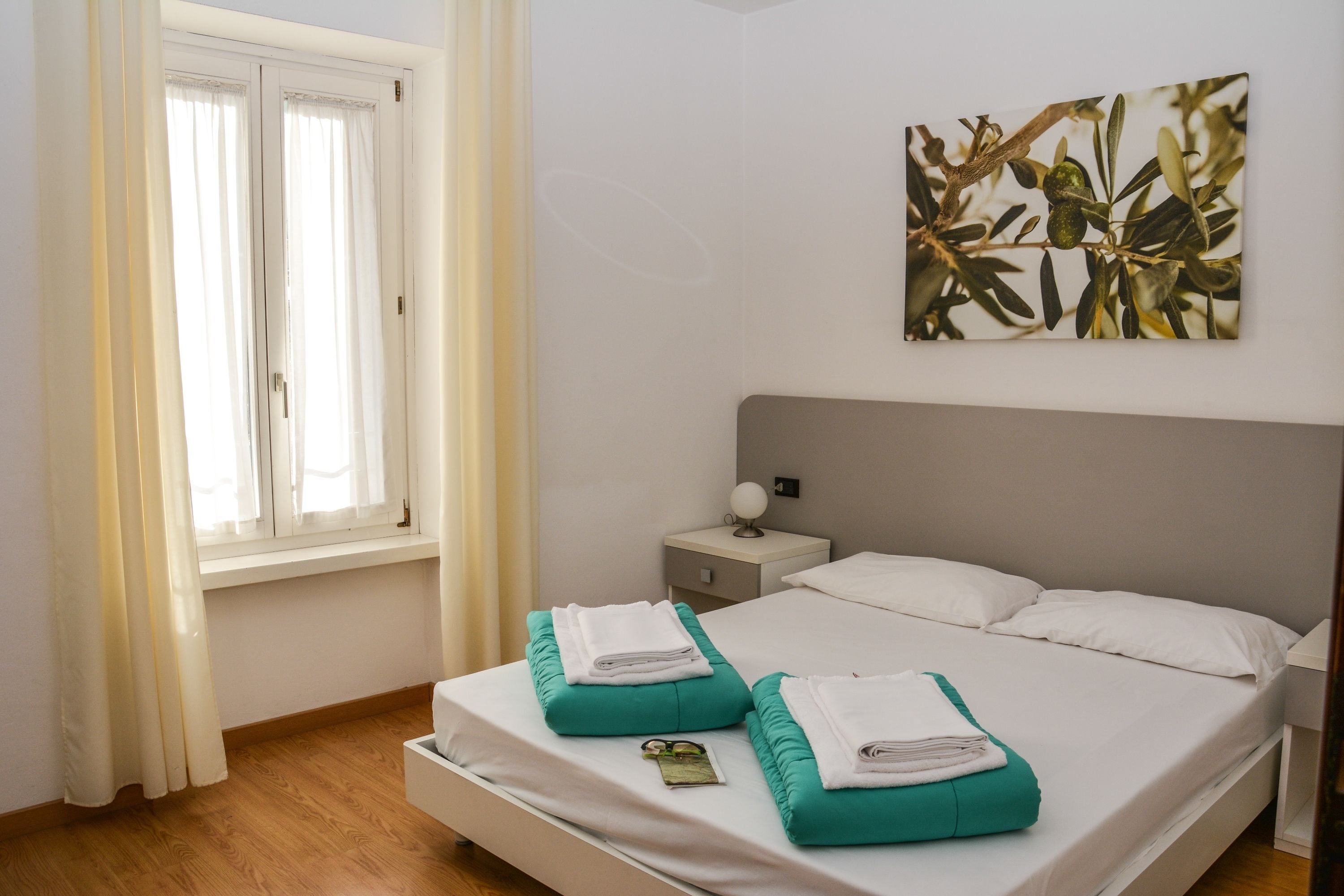 Ein Schlafzimmer mit einem Bett, zwei Kissen, einem Nachttisch, einer Lampe und einem Fenster mit Vorhängen.