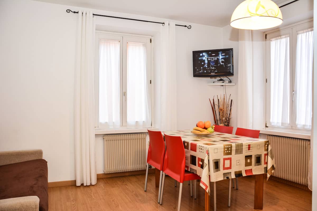 A dining area with a table, chairs, a television, and a window with curtains.