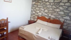 A bedroom with a stone wall, a wooden bed frame, a white bedspread, and a wooden chair. - Bungalows Bela Vista Maio Beach (Maio)