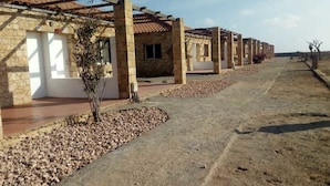 A row of stone buildings with a pergola over a patio area, surrounded by gravel and a clear sky. - Bungalows Bela Vista Maio Beach (Maio)