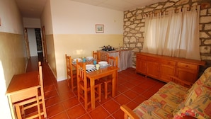 A compact living space with a dining area, a kitchenette, a sofa, and a stone wall. - Bungalows Bela Vista Maio Beach (Maio)