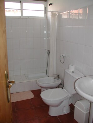 Un baño con bañera, dos inodoros, lavabo y cortina de ducha.