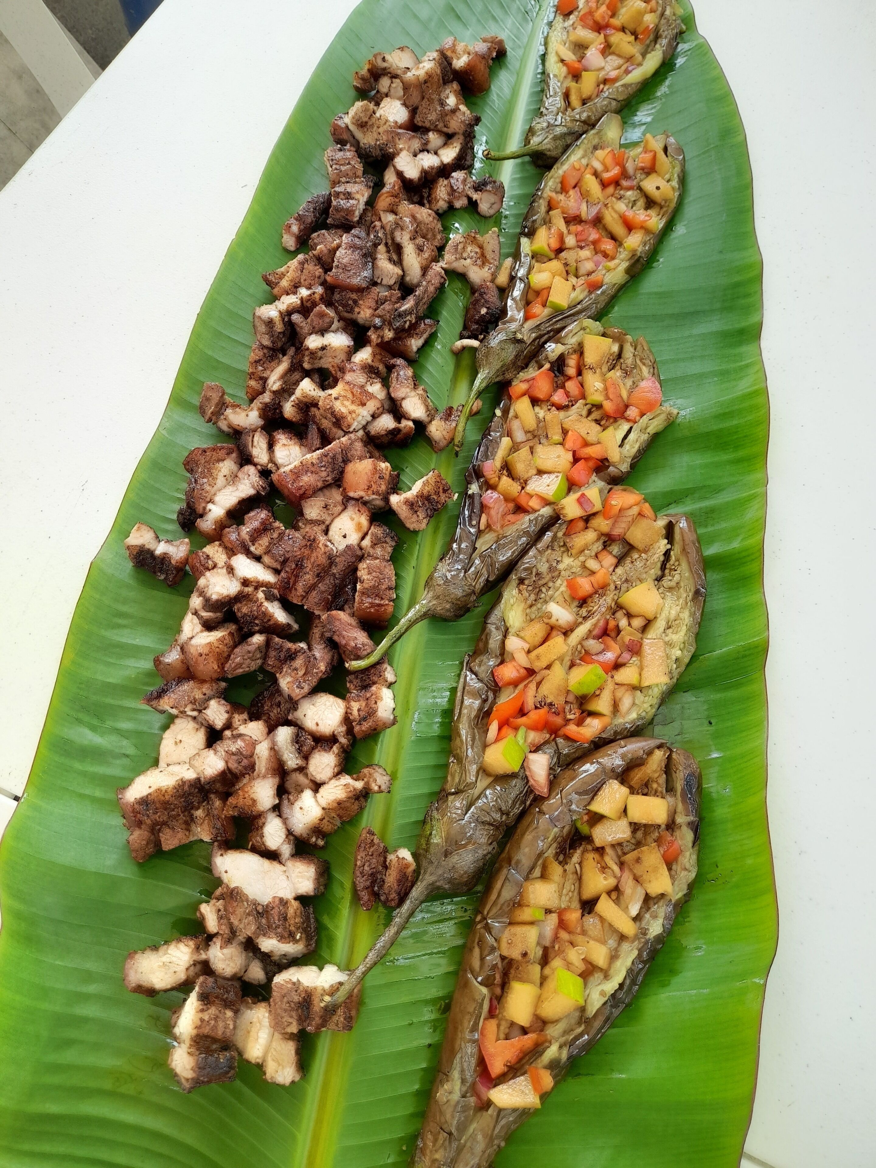 A plate of grilled meat and stuffed vegetables on a banana leaf.