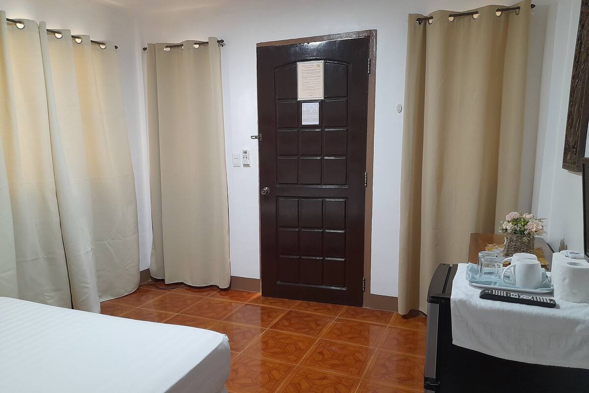 A hotel room with a bed, a table with a tray of items, a door with a notice, and curtains.