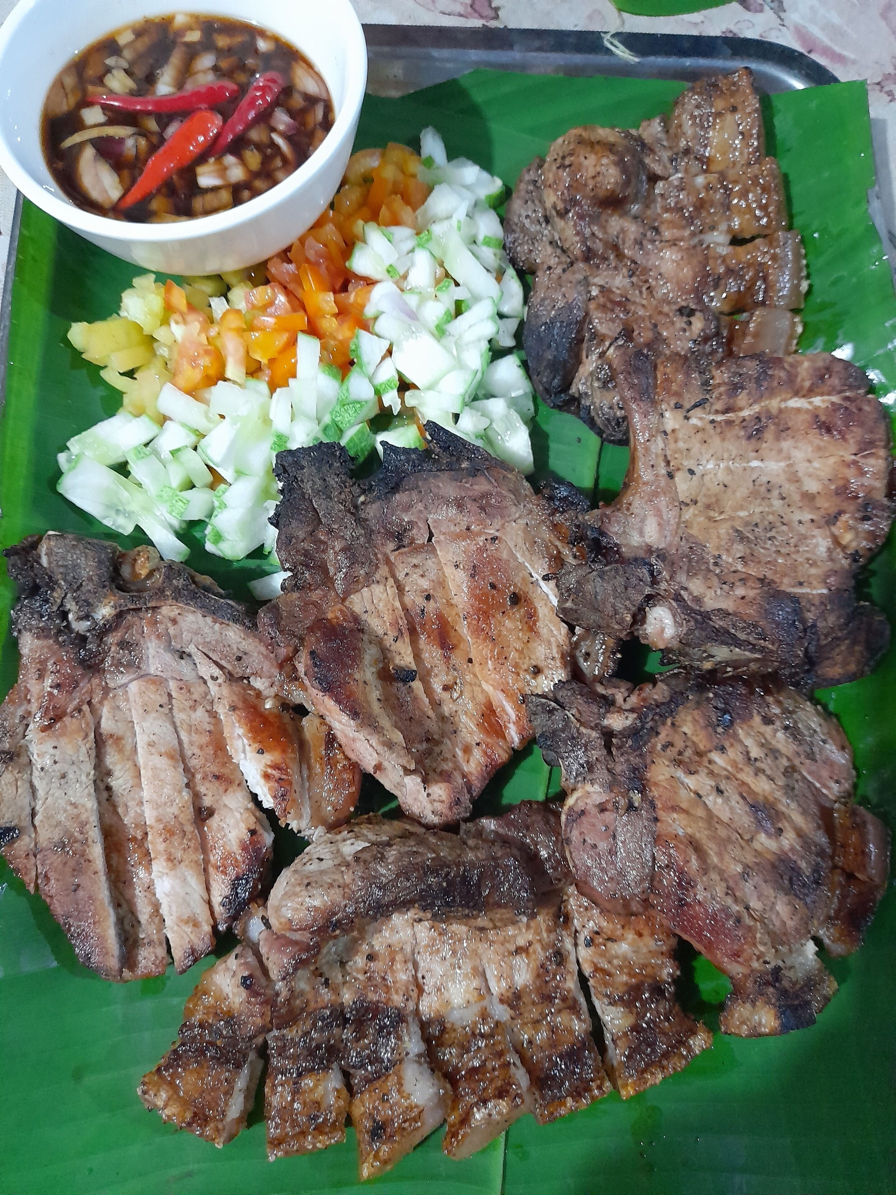 A plate of grilled meat with a side of diced vegetables and a bowl of sauce.