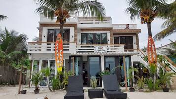A modern two-story building with a balcony, palm trees, and lounge chairs.