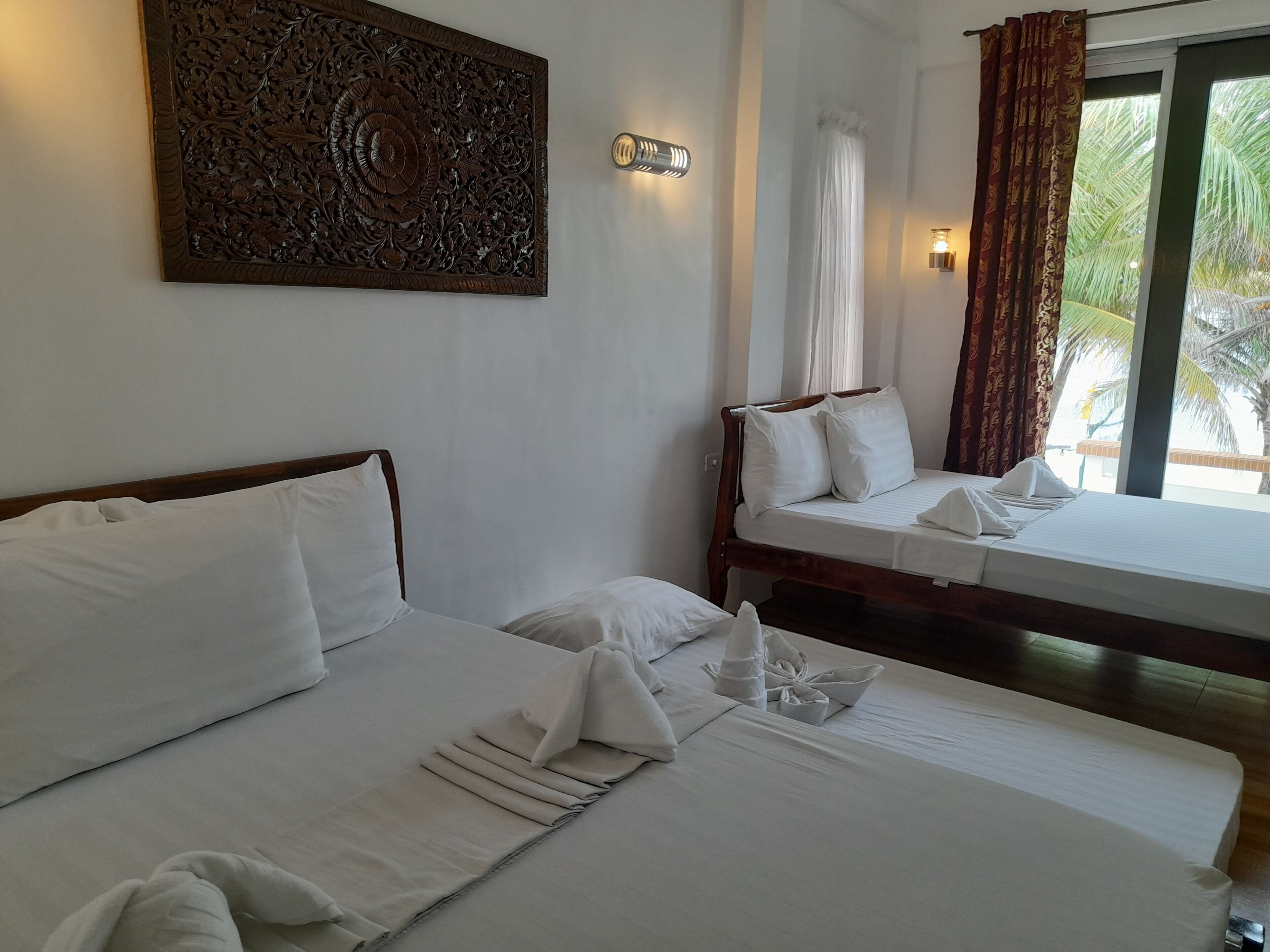Une chambre d’hôtel avec deux lits, un panneau décoratif au mur et une vue sur les palmiers par la fenêtre.