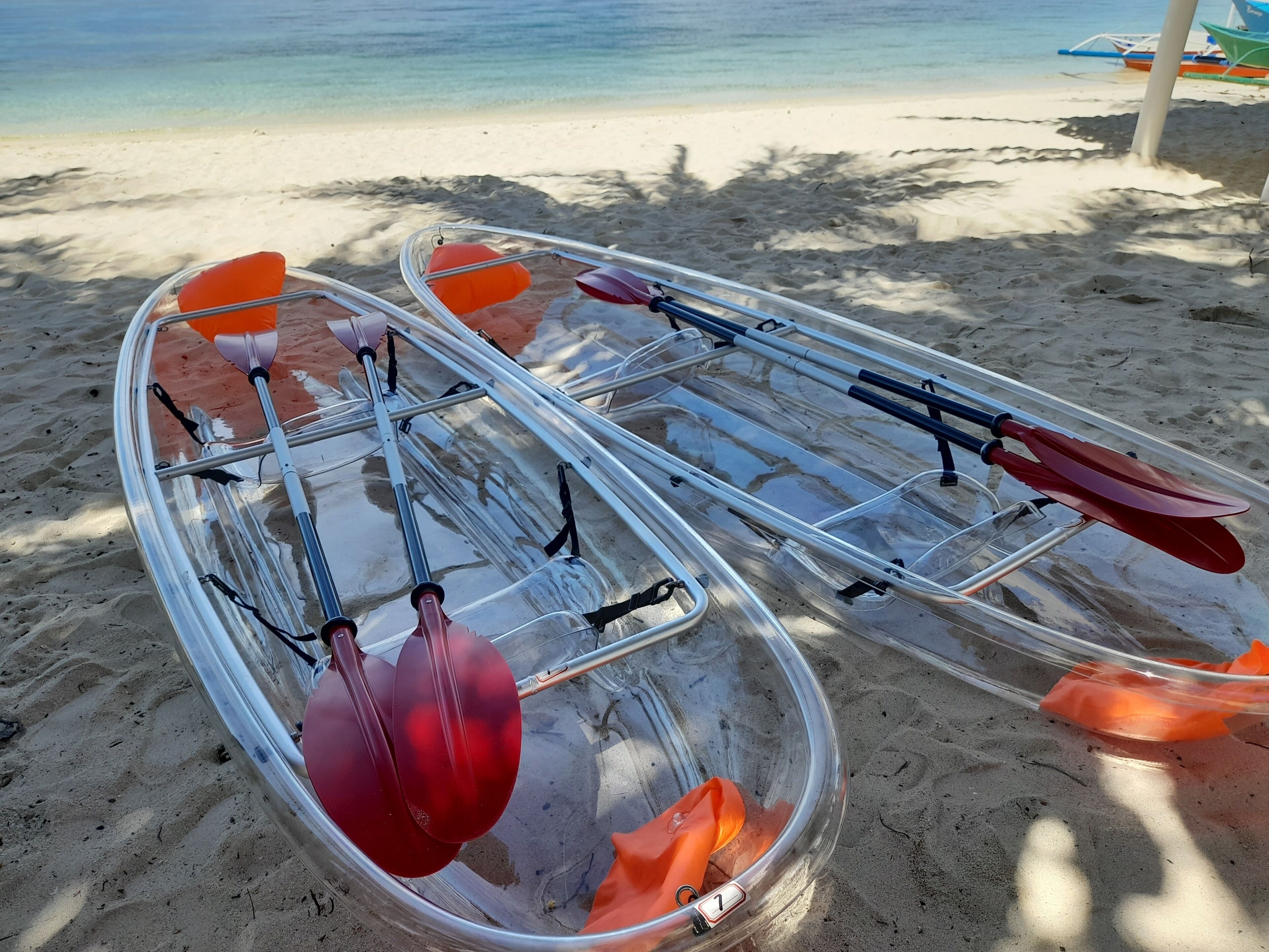 Two kayaks with paddles and orange flotation devices on a sandy beach.