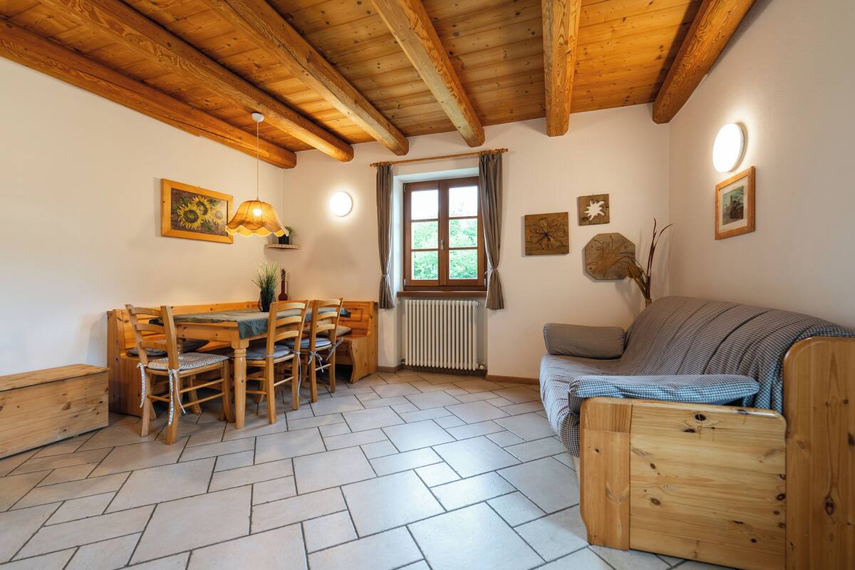 Um quarto aconchegante com teto de madeira, uma mesa de jantar com cadeiras, um sofá e um radiador.