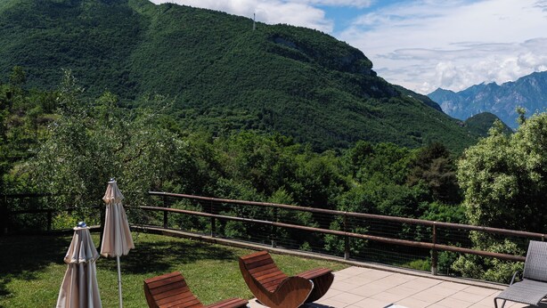 A swimming pool with lounge chairs and umbrellas, surrounded by lush greenery and mountains. - Maso Salim (Drena)