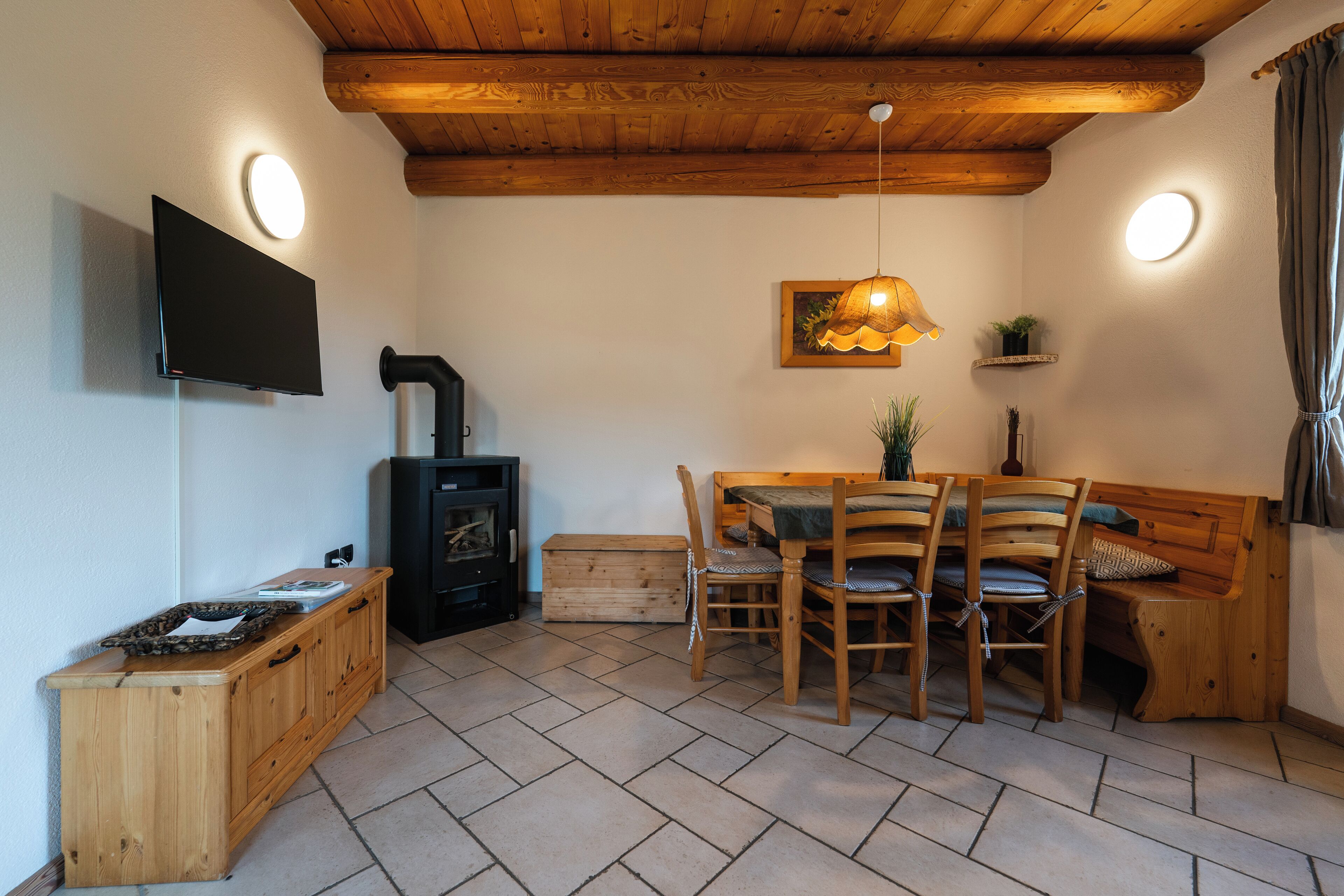 Een knus interieur met een houten plafond, een flatscreen televisie aan de muur, een houten eettafel met stoelen, een bankje en een open haard.