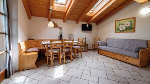 A cozy room with a wooden ceiling, a sofa, a dining table with chairs, and a TV mounted on the wall. - Maso Salim (Drena)