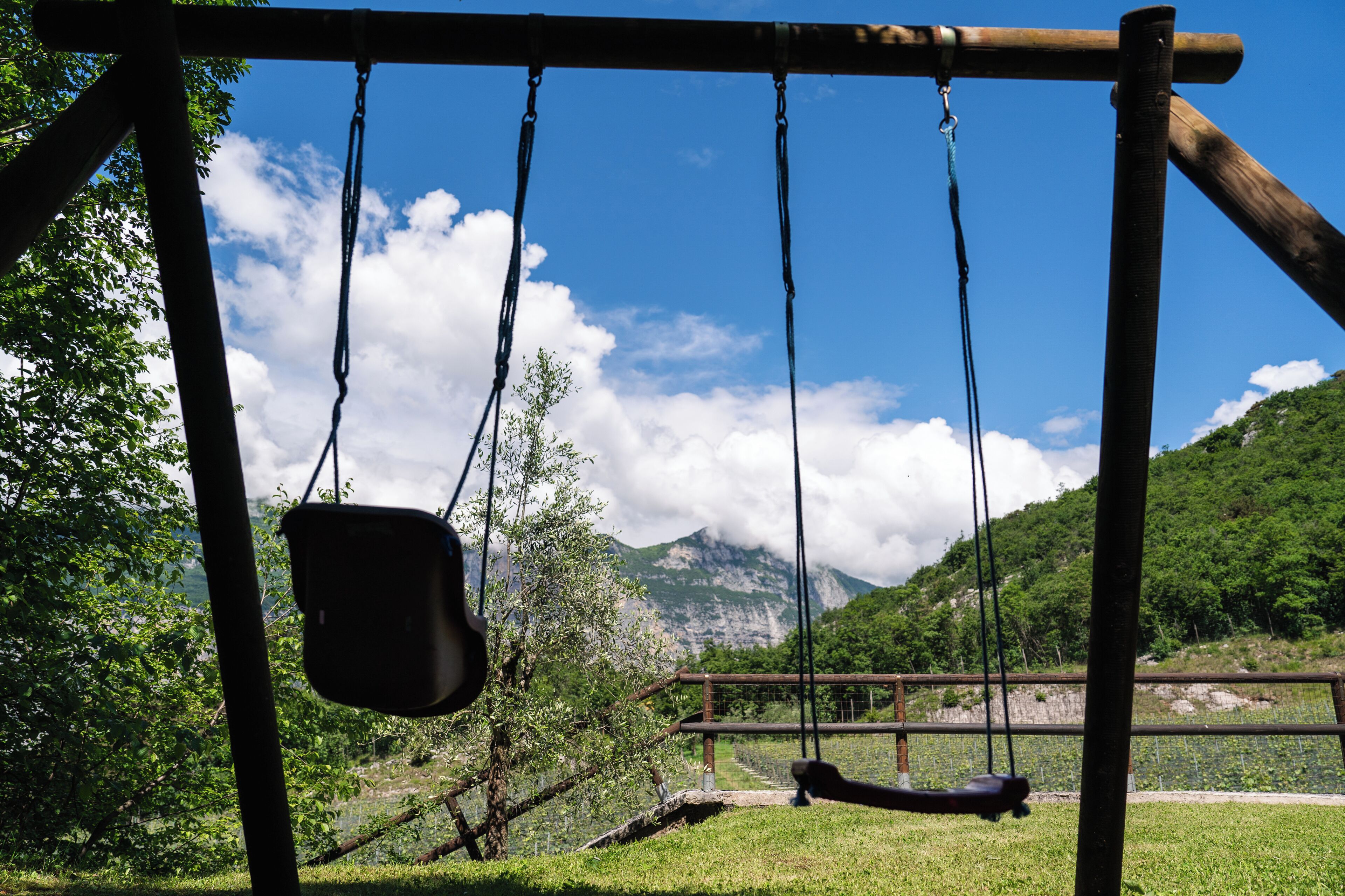 Un columpio de madera en un área con césped y montañas al fondo.