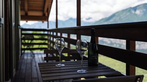 A wooden table with two wine glasses and a bottle of wine on a balcony overlooking mountains. - Maso Salim (Drena)