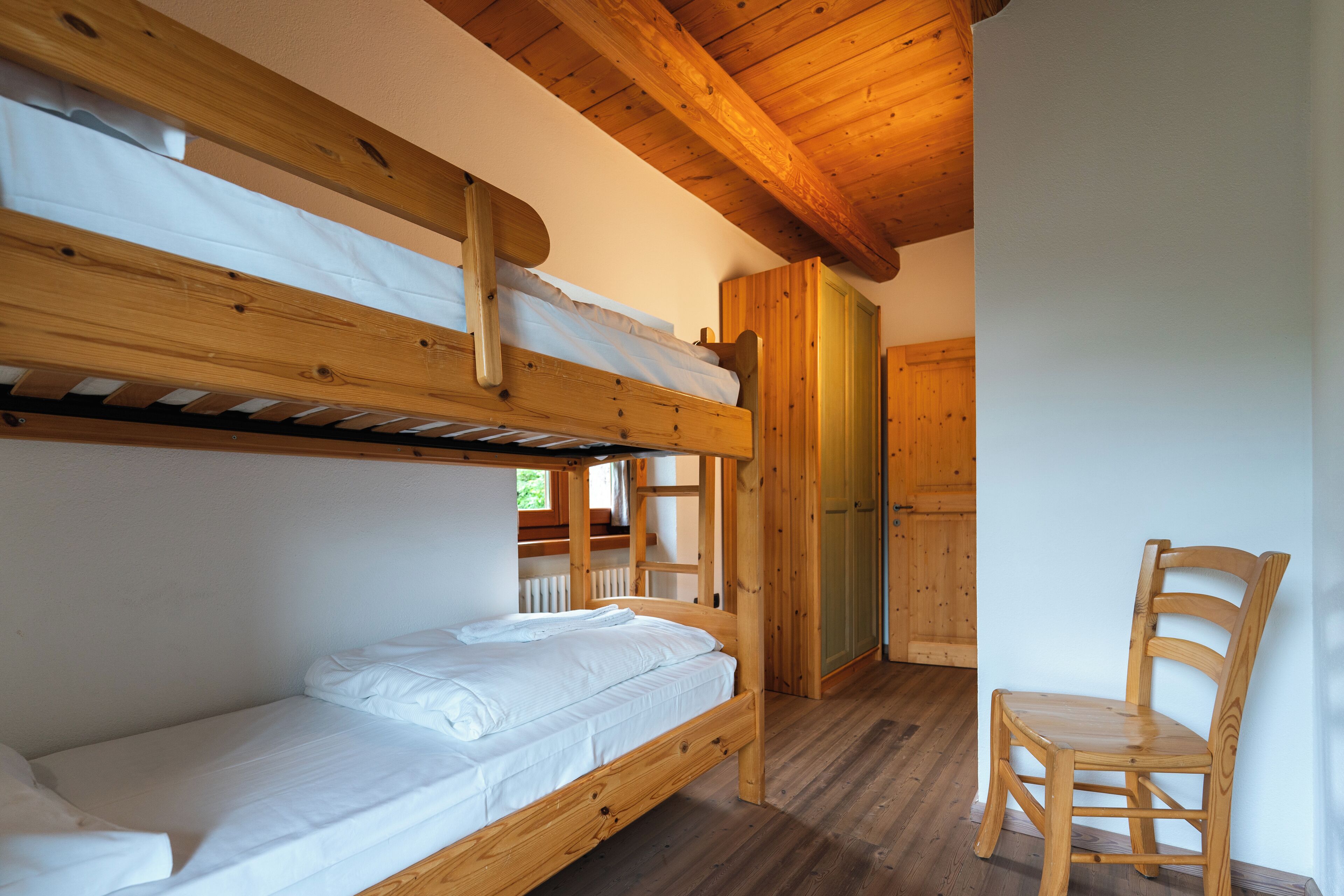 A bunk bed room with a wooden chair and a door.