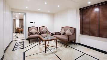 A room with two sofas, a glass-top coffee table, and a window with blinds.