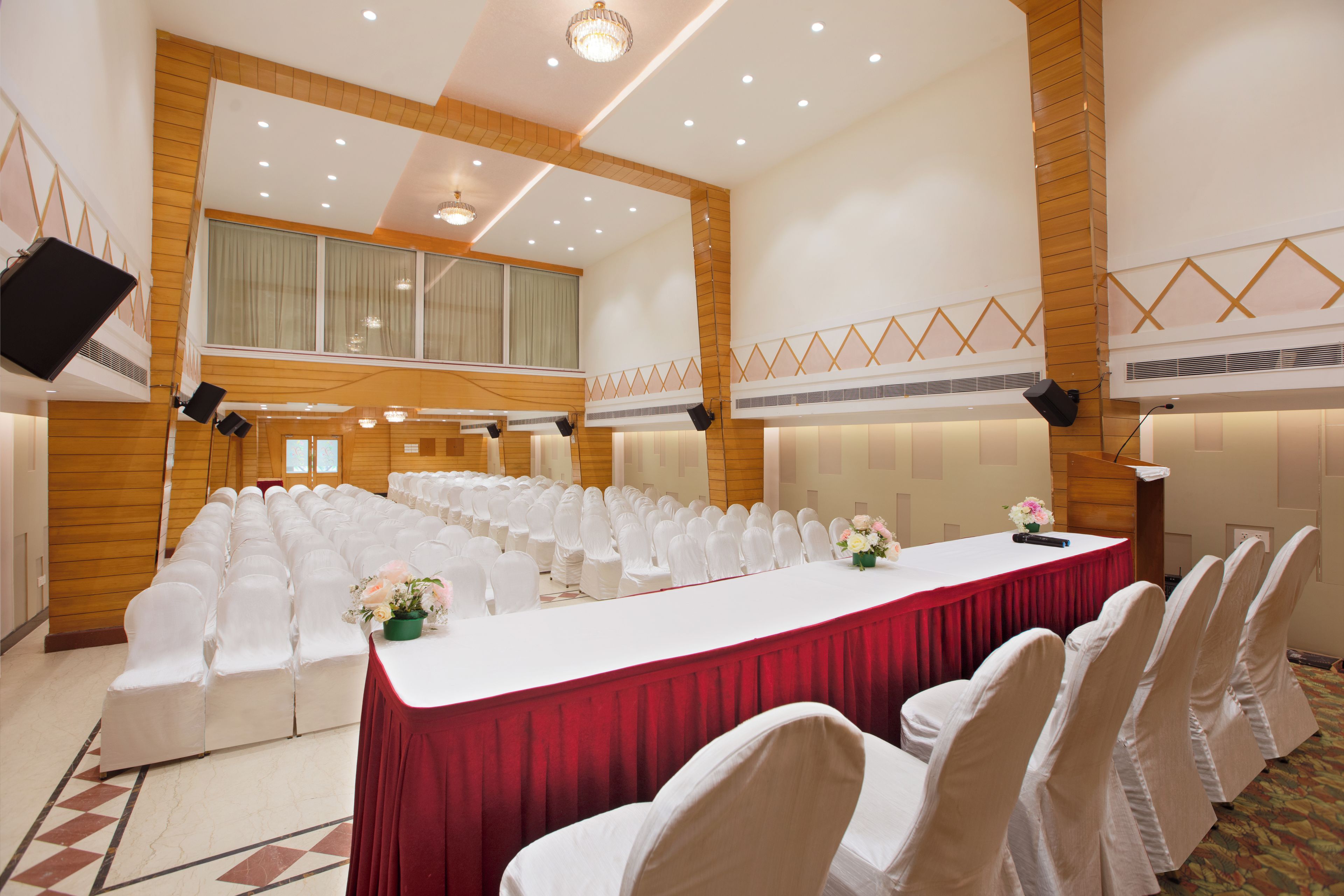 A conference room with rows of white chairs, a long table with a red tablecloth, and a large chandelier.