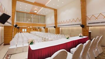 A conference room with rows of white chairs, a long table with a red tablecloth, and a large chandelier.