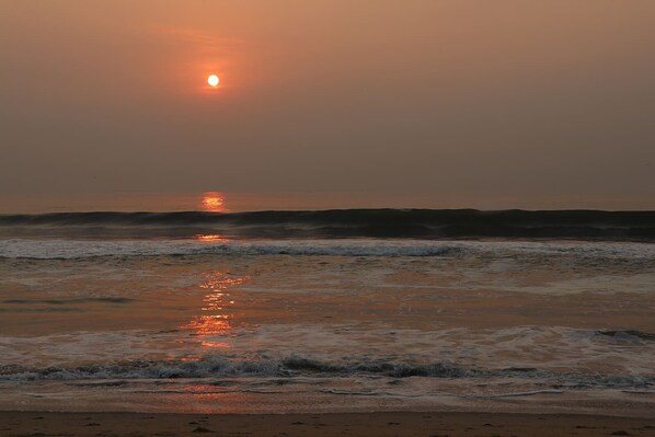 Atardecer sobre el océano con olas reflejando la luz del sol.