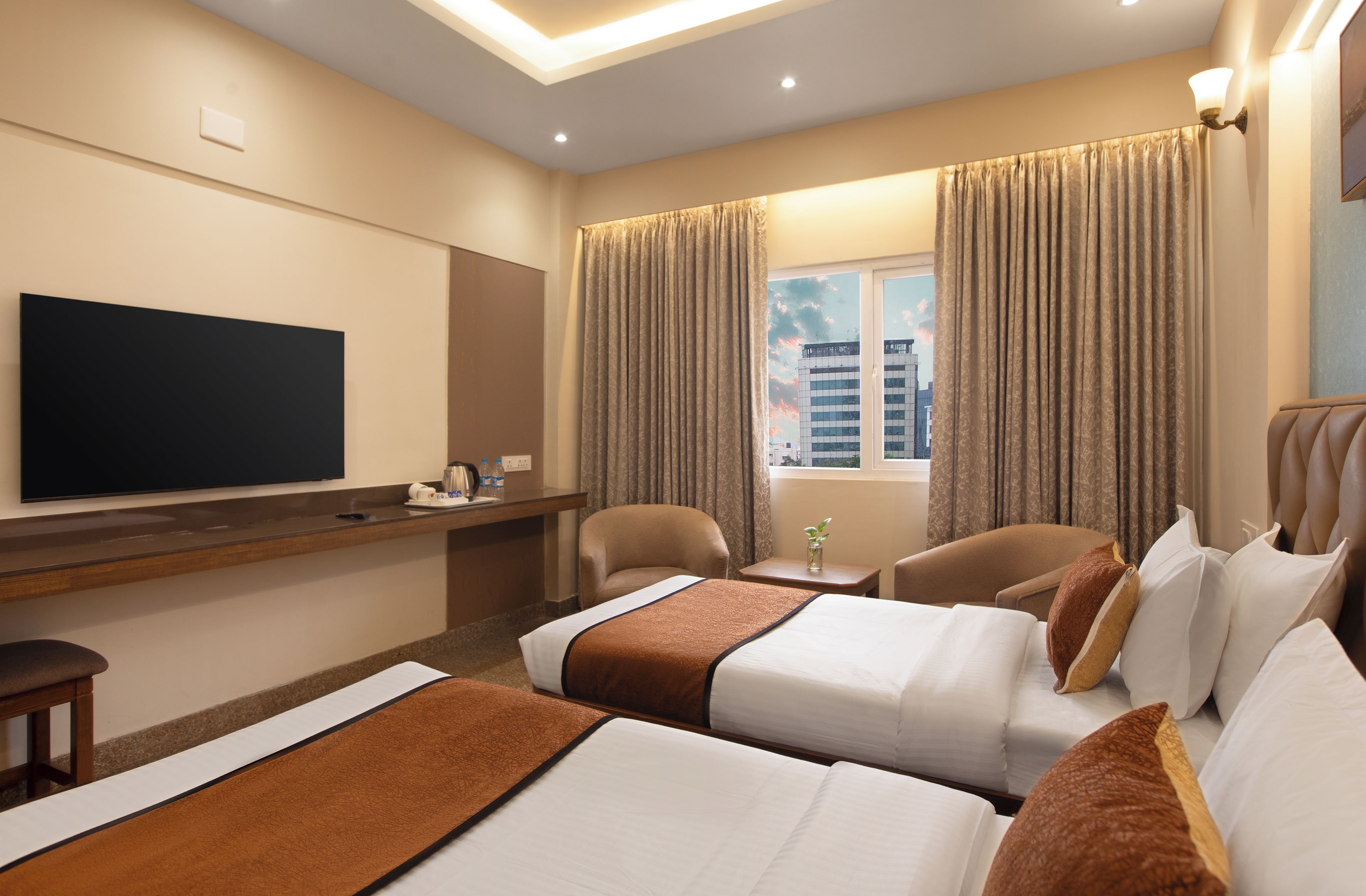 A hotel room with two beds, a TV, a desk, and a window with curtains.