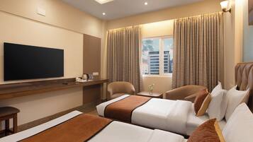 A hotel room with two beds, a TV, a desk, and a window with curtains.