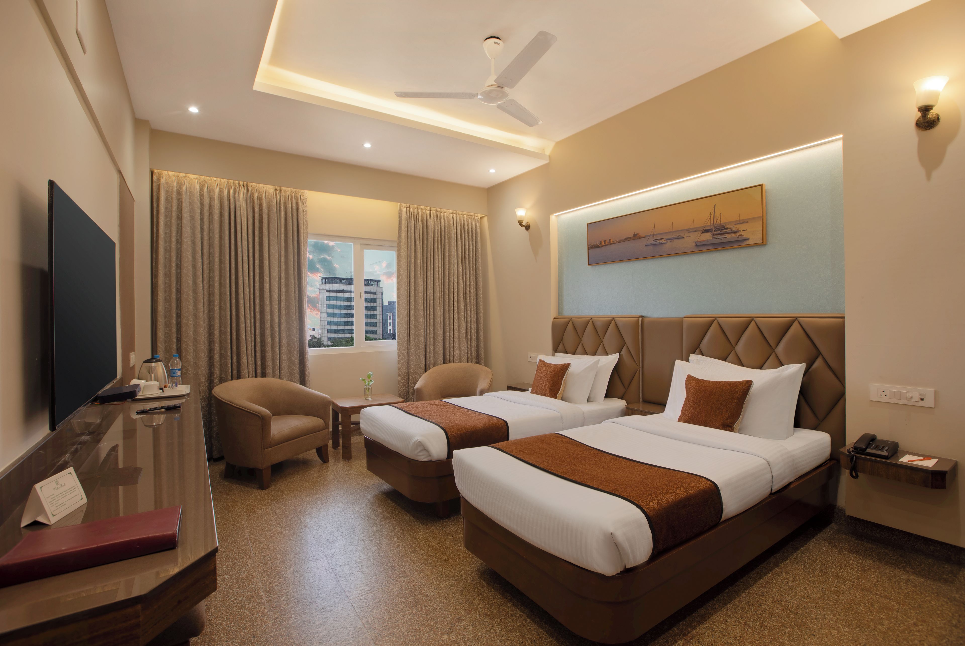 A hotel room with two beds, a desk, a chair, a TV, and a window with curtains.
