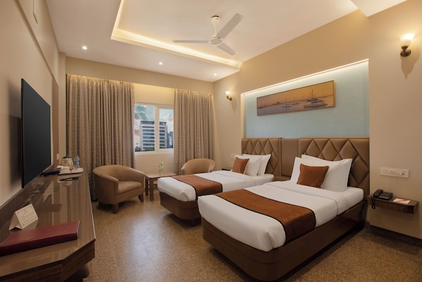 Habitación de hotel con dos camas, un escritorio, una silla, un televisor y una ventana con cortinas.
