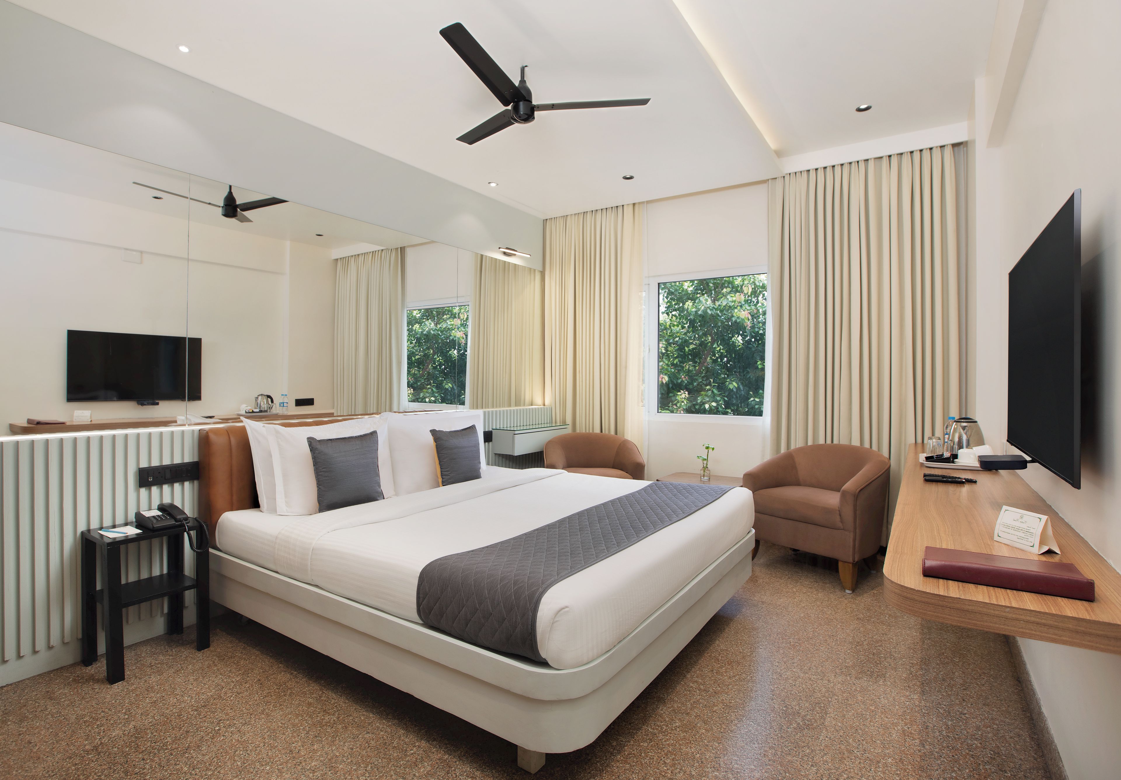 Una habitación de hotel moderna con una cama grande, un escritorio, una silla, un televisor y un ventilador de techo.