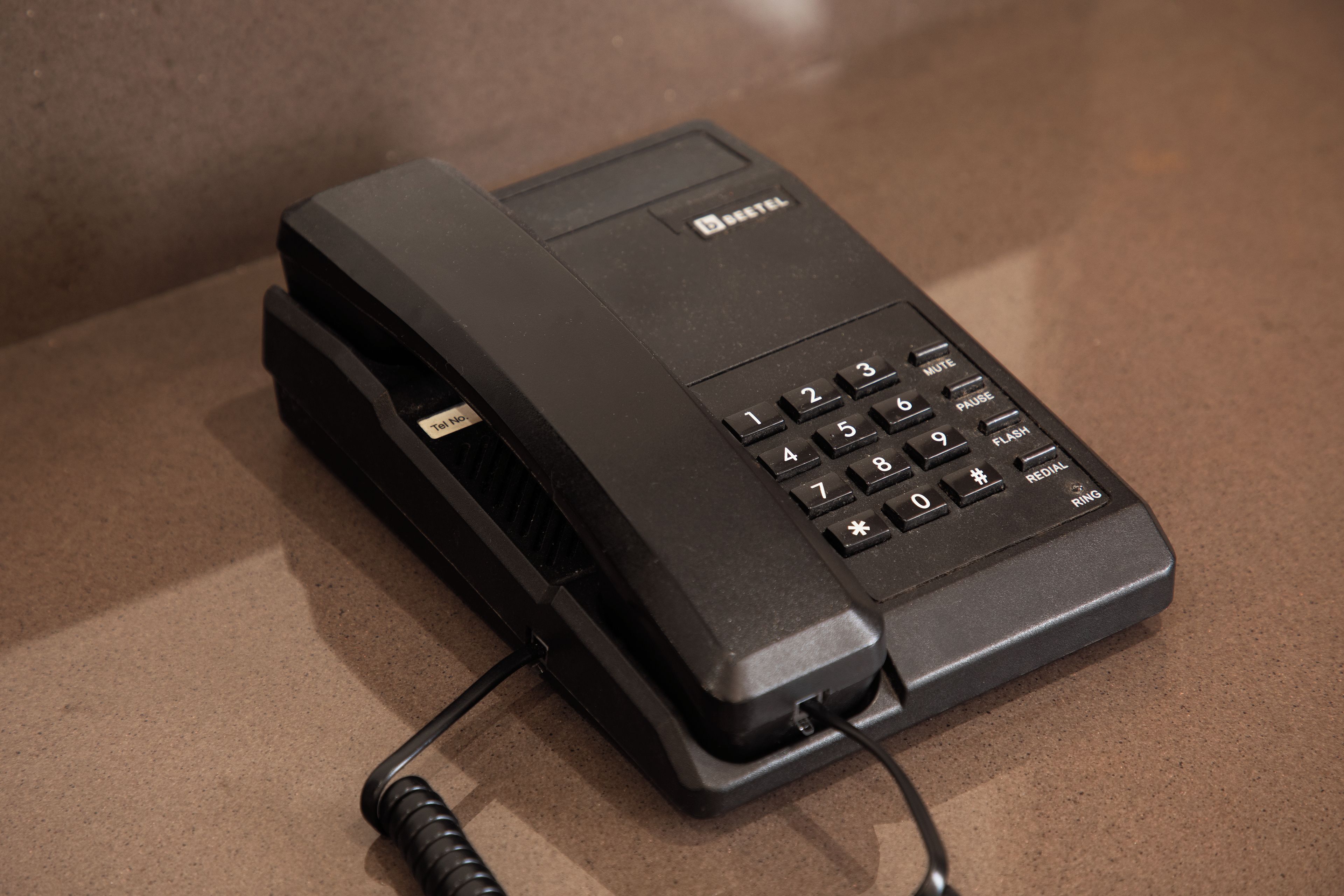 A black telephone with a cord, placed on a brown surface.