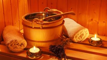 Uma sauna de madeira com uma grande banheira de madeira, duas toalhas enroladas e duas velas acesas.