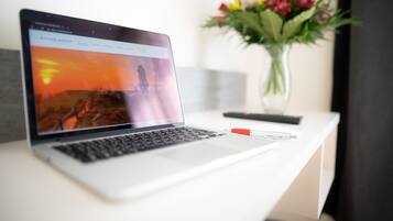Een laptop op een wit bureau, met op de achtergrond een vage zonsondergang en een boeket bloemen.