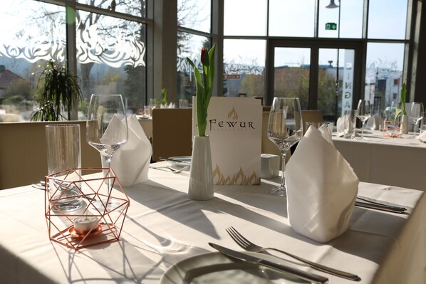 Mesa lista para comer en un restaurante, con un atril para el menú, un candelabro y un florero con una flor.