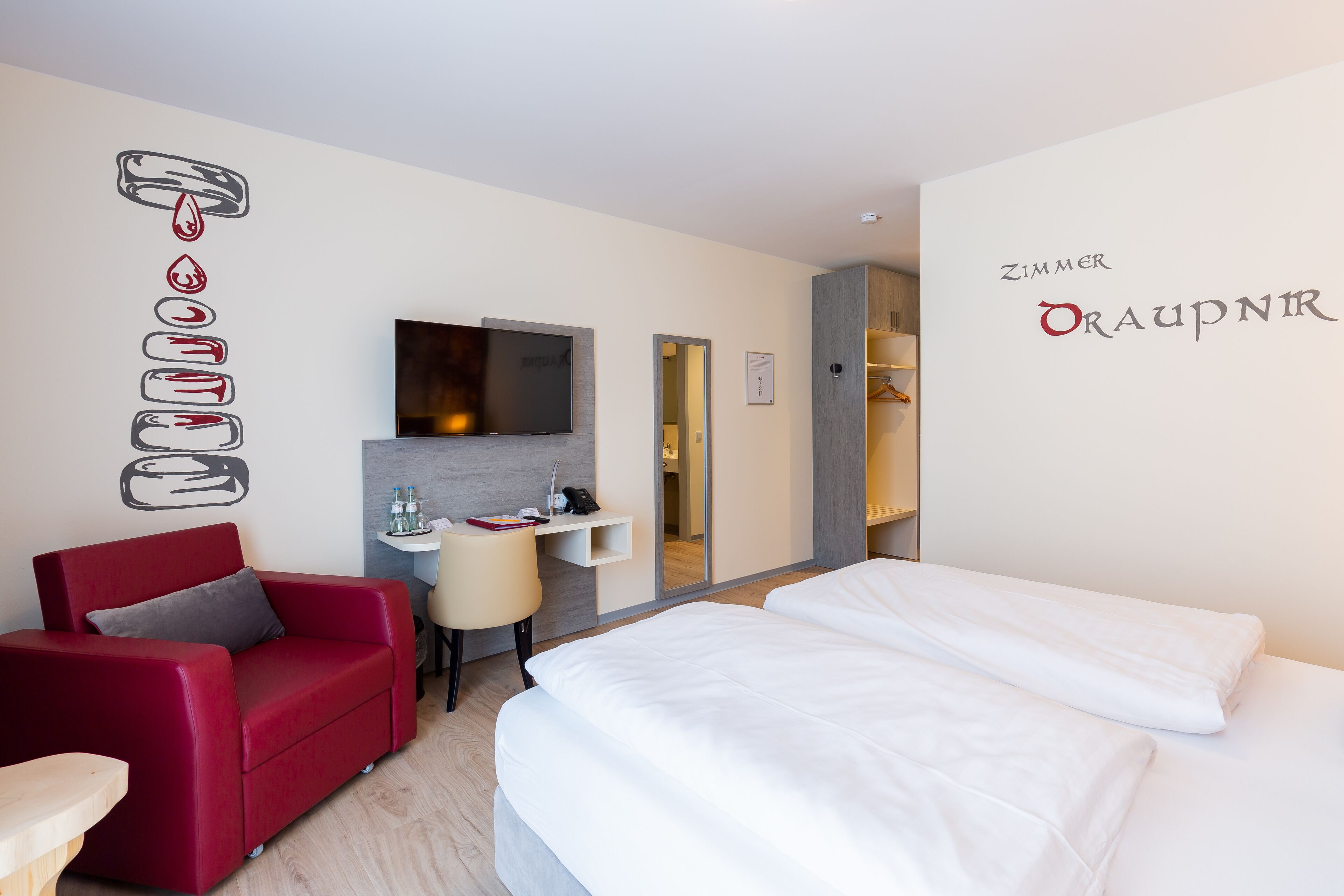 Une chambre d’hôtel avec un canapé rouge, un lit, une télévision, un bureau et un miroir.