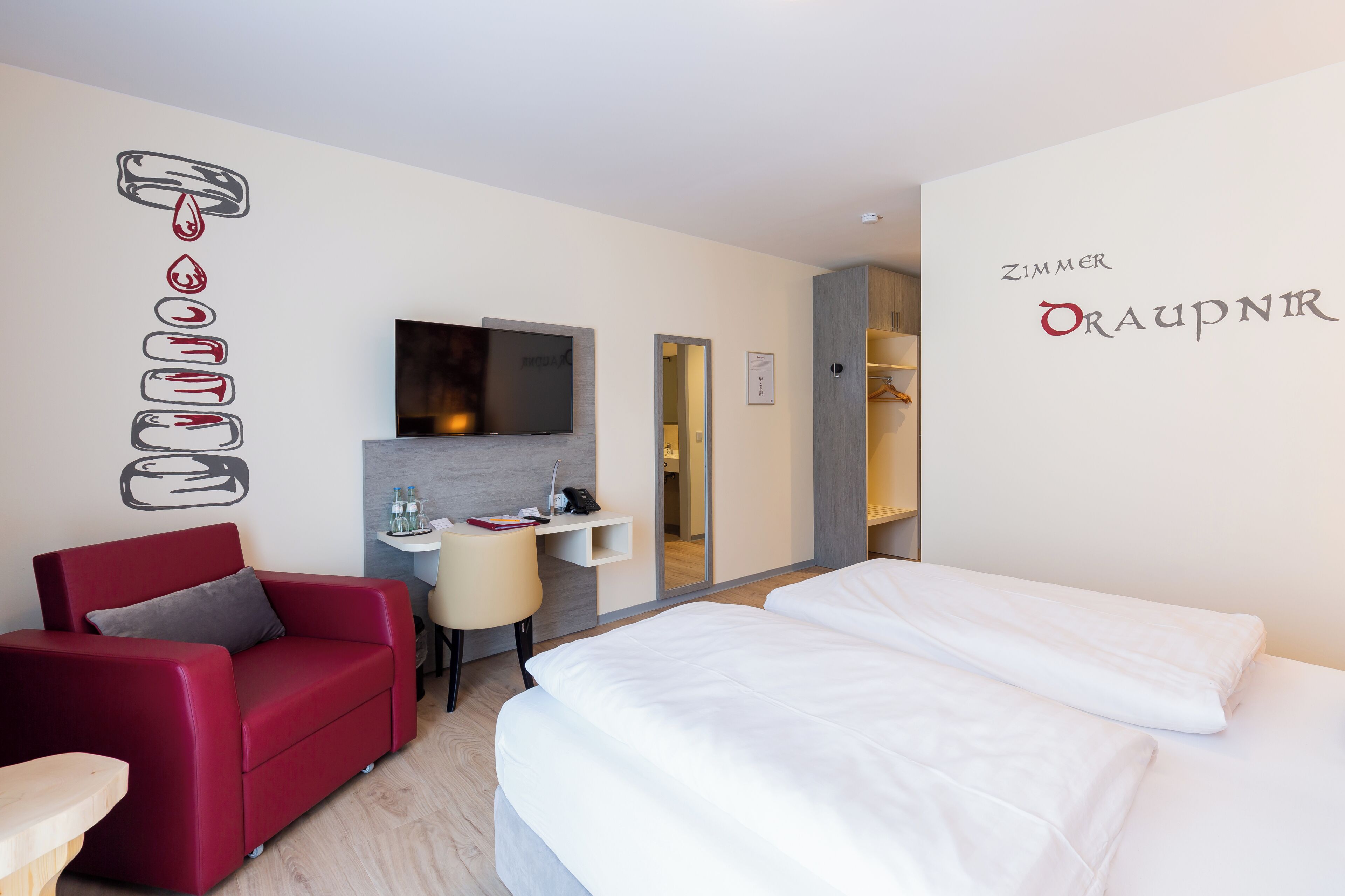 A hotel room with a red sofa, a bed, a TV, a desk, and a mirror.