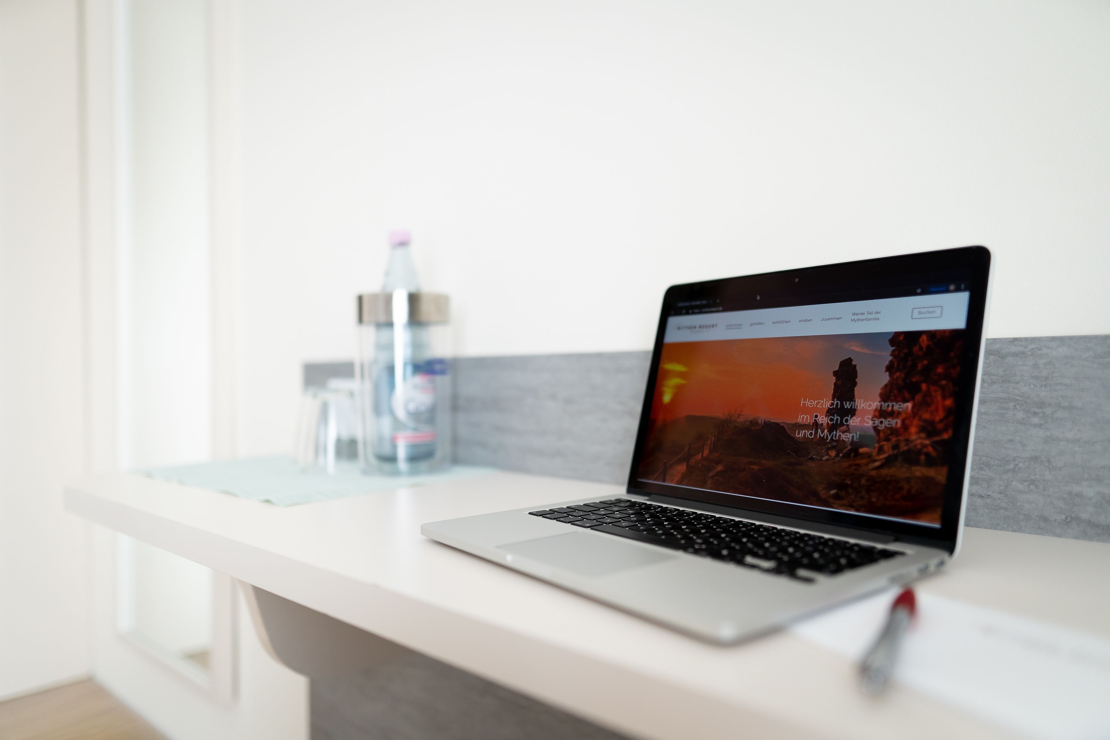 A laptop on a white desk with a water bottle and a glass of water in the background.