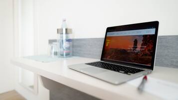 A laptop on a white desk with a water bottle and a glass of water in the background.