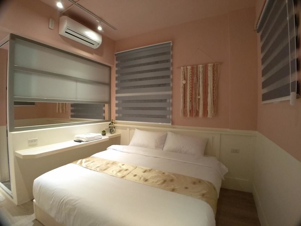 Une chambre à coucher comprenant un lit, une table de chevet, un miroir, une fenêtre avec des stores et un appareil de climatisation.