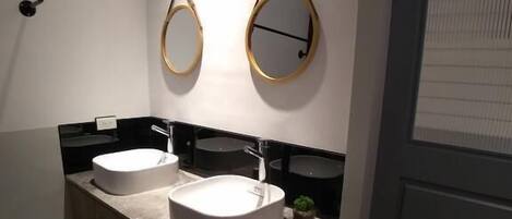A modern bathroom with two sinks, a towel rack, and a small potted plant.