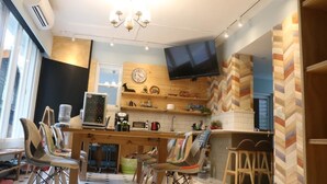 A modern kitchen with a wooden countertop, a built-in oven, a microwave, and a television mounted on the wall. There are chairs and stools around the kitchen area. - itravel Hostel (Hualien City)