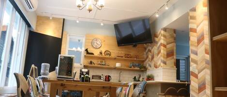 A modern kitchen with a wooden countertop, a built-in oven, a microwave, and a television mounted on the wall. There are chairs and stools around the kitchen area.