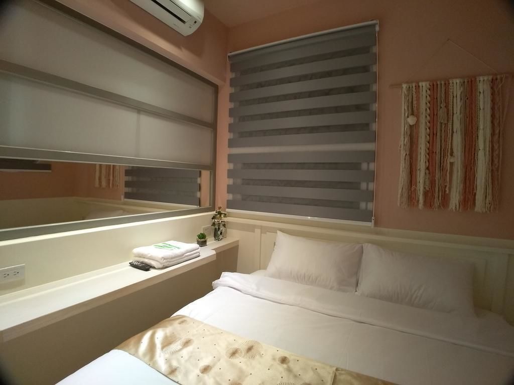 A hotel room with a bed, a bedside table with a lamp, a window with blinds, and a wall-mounted air conditioner.