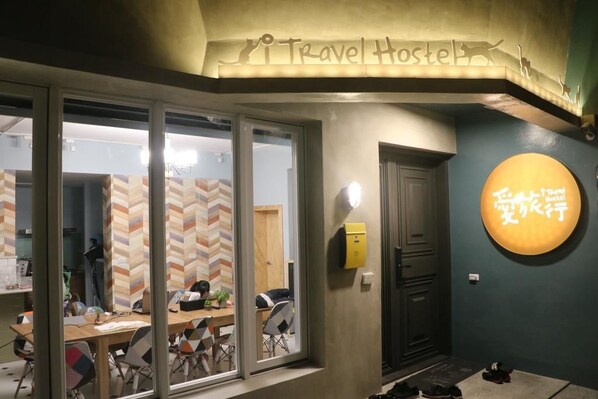 Un hostal de viajes con una pared de diseño en zigzag, un escritorio de madera con sillas y un letrero de neón con caracteres chinos.