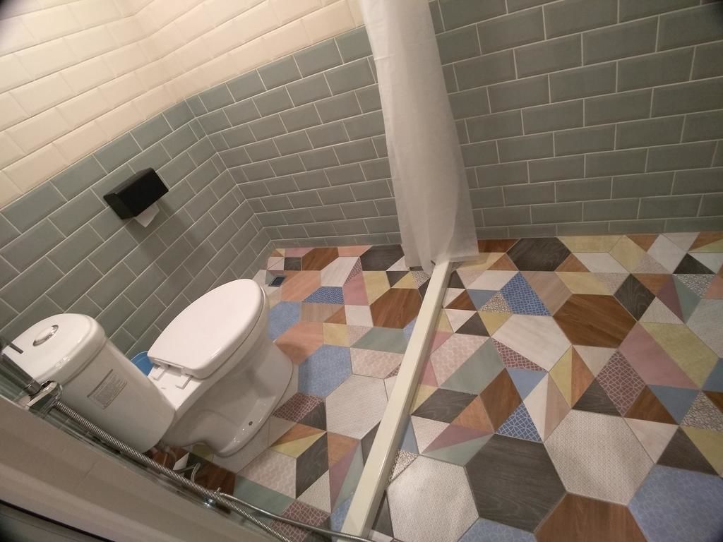 A bathroom with a toilet, a shower curtain, and a tiled floor with a geometric pattern.