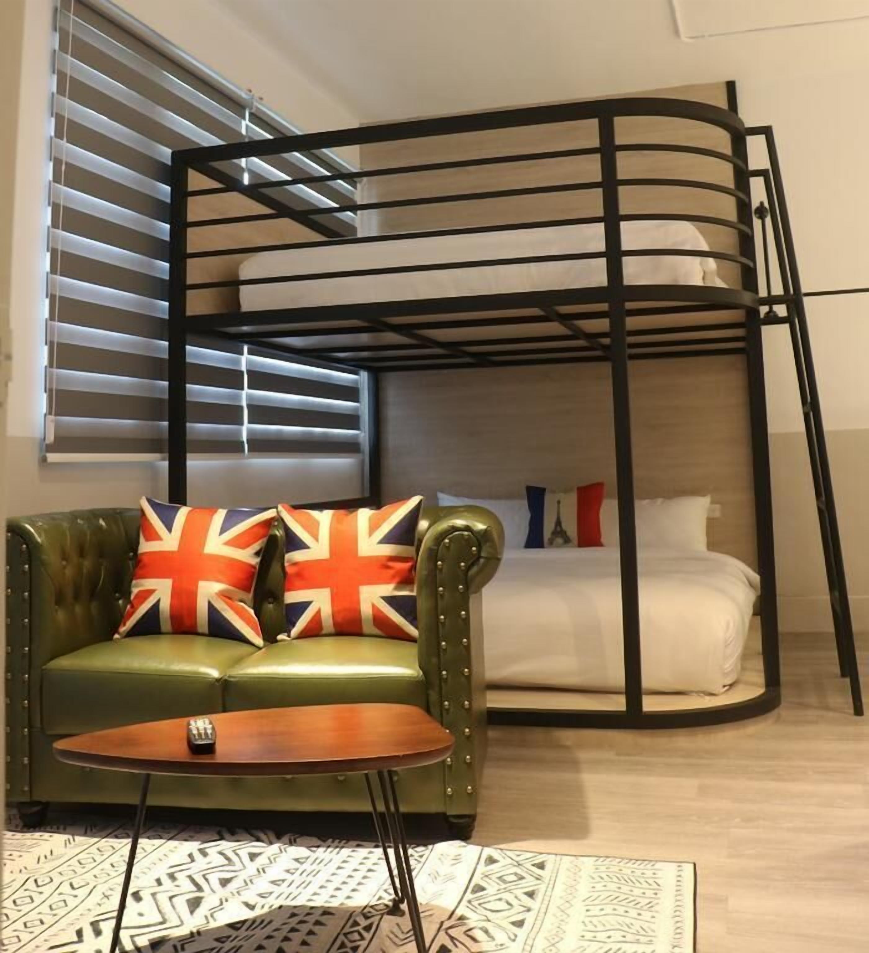 Una cama litera con un sofá de cuero verde y una mesita pequeña al frente, una alfombra estampada y una ventana con persianas.