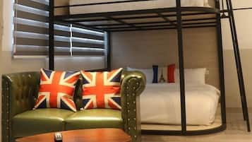 A bunk bed with a green leather sofa and a small table in front, a patterned rug, and a window with blinds.