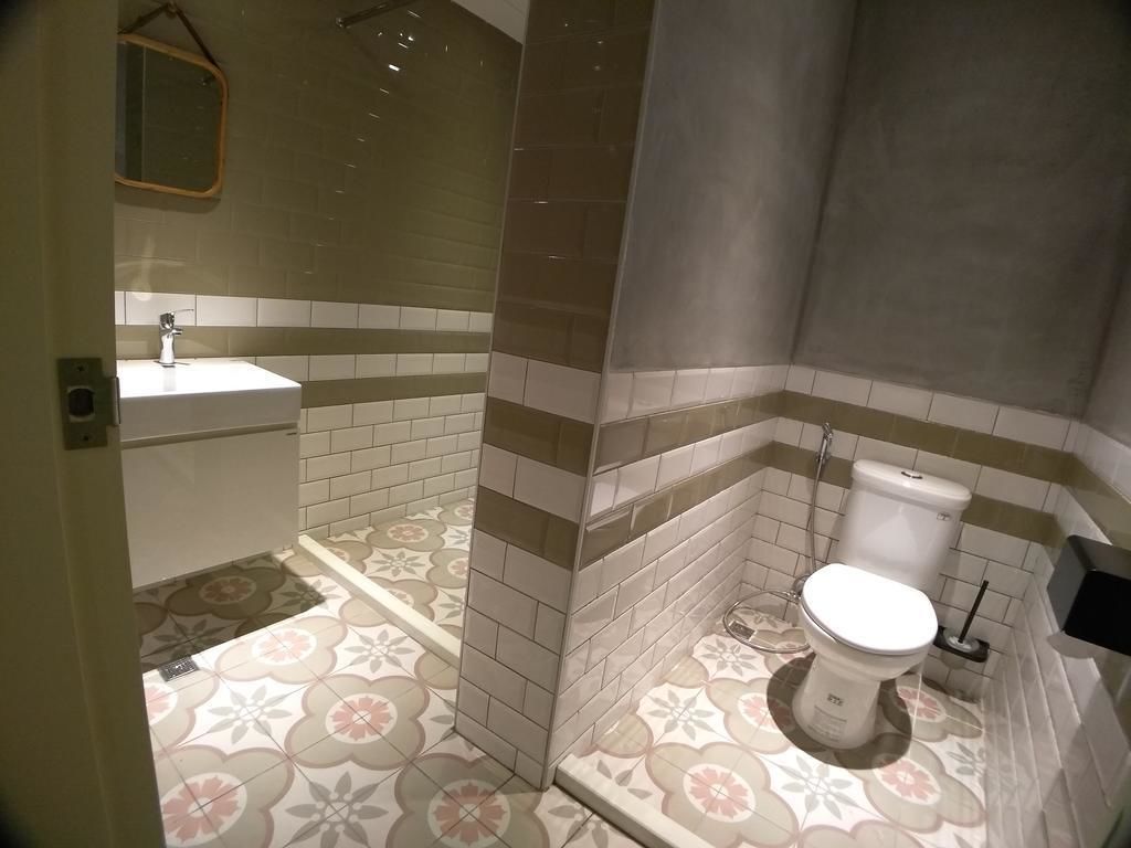 Un baño con ducha, inodoro y lavamanos, con azulejos estampados y un espejo.